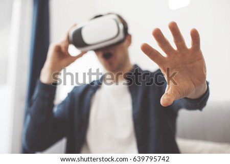 Excited man feeling inside virtual reality. Using VR headset and watching video in bright white studio