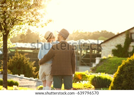 A couple in love at sunset in hats stand with their backs in the frame. American dream. A retro couple in his country house, his estate. Lavstory, family day, St. Valentine's Day.