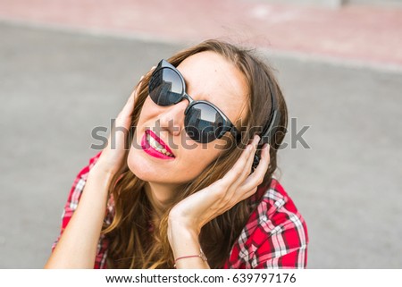 Young smiling woman relaxing and listening to music with headphones in the street.