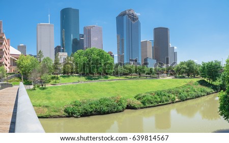 Panorama view downtown Houston taken from pedestrian bridge at daytime, cloud blue sky. Green lawn, trees, modern skylines along Bayou river. Most populous city in Texas, fourth-most in United States.
