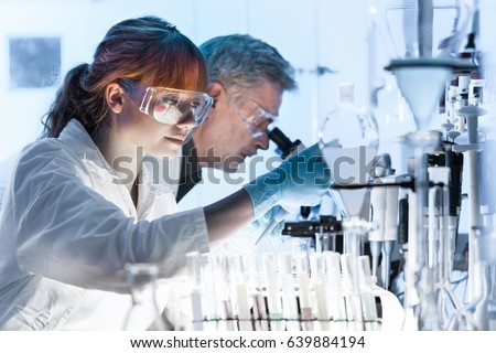 Health care researchers working in life science laboratory. Young female research scientist and senior male supervisor preparing and analyzing microscope slides in research lab. Royalty-Free Stock Photo #639884194