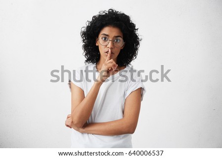 Human facial expressions and emotions. Anxious young mother with dark skin and black curly hair dressed casually keeping index finger at her lips asking not to make noise while her baby is asleep