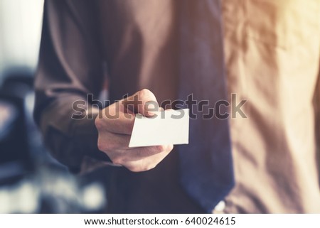 Business man holding white business card in the office. Vintage toned.