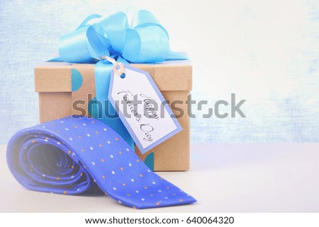 Happy Fathers Day gift and neck tie on white wood table and pale blue background, with applied retro style filters.