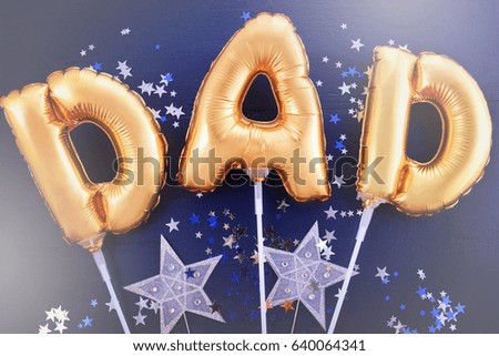 Happy Fathers Day gold baloons for the word, Dad, on dark blue wood background with silver and blue scattered glitter stars, with applied retro style filters.