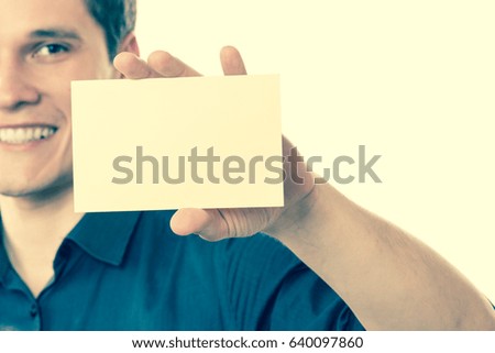 Advertisement concept. Young handsome man holding blank piece of paper. Smiling guy showing empty ad. Filtered.