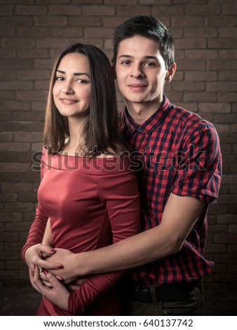 Happy young woman and man in love stand and smile in a red brick studio