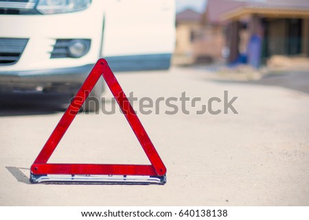 Red broken stop triangle sign on asphalt and blurred car against