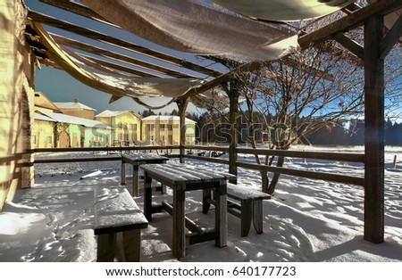 Wooden table and benches covered with snow under the tent in the background of the medieval village by night