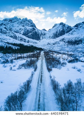 Aerial shot of snowy forest and road leading to majestic mountain. Lofoten Islands, Norway.