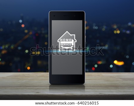 Hammer and wrench with house icon on modern smart phone screen on wooden table over blur colorful night light of city tower, Home service concept