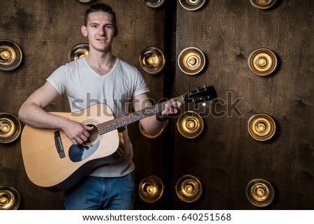 Guitarist, music. A young man plays an acoustic guitar on a background with lights behind him