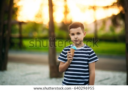 A little boy in a striped T-shirt is eating blue ice cream.Spring, sunny weather.