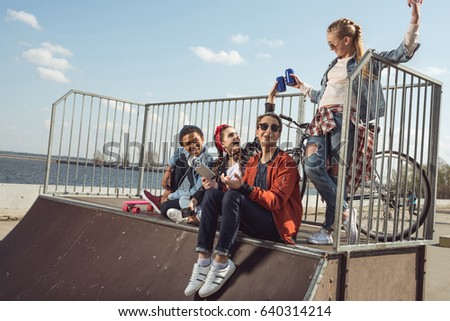 teenagers having fun with smartphone in skateboard park, hipster students concept
