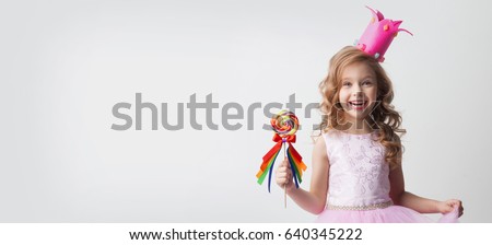 Small princess girl in crown holds a large spiral decorated lollipop candy Royalty-Free Stock Photo #640345222
