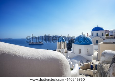 Iconic blue church domes in Oia, Santorini, Greece on a summer day with a cruise ship in the background. 
