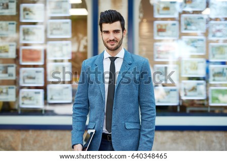 Outdoor portrait of confident, young real estate agent standing front of agency.