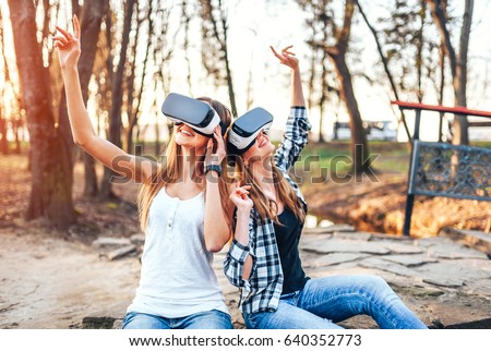 Two young girls enjoy virtual reality glasses outdoor