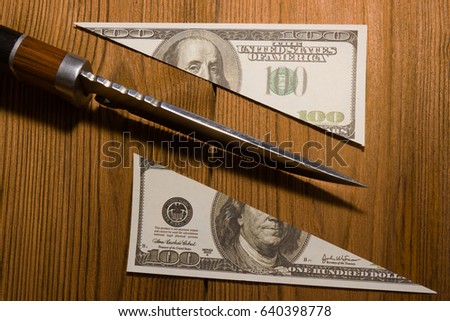 The concept of money is to divide into two halves, to cut banknotes with a hundred dollars with a knife. The cut banknote lies on a wooden board. Natural material. Business, crime. Property division.