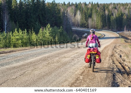 Girl, young woman riding a bicycle in a helmet on the asphalt road with a bike rack. In the background there is a forest, a forest road. Cycling, traveling on bicycles.