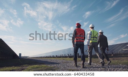 Technician walks with workman and investor through field of solar panels Royalty-Free Stock Photo #640433458