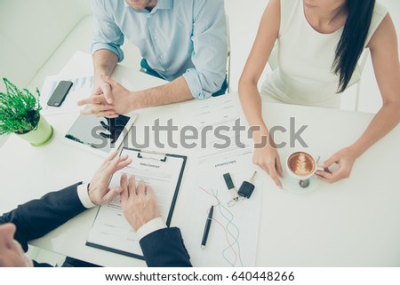 Cropped photo of couple getting a car key from a car dealer in the showroom and signing contract