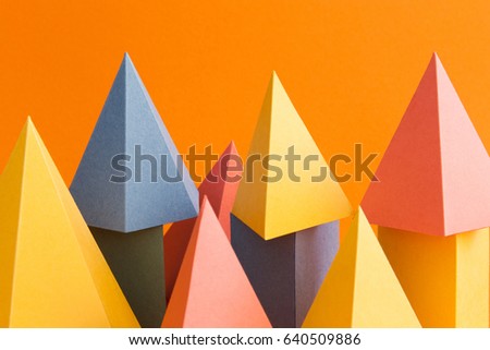 Abstract colorful geometrical background. Three-dimensional prism pyramid objects on orange paper. Yellow blue pink green colored solid figures, soft focus photo.