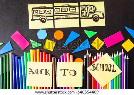 Back to school background with a lot of colorful felt-tip pens and colorful pencils, titles "Back to school" and drawing of school bus drawn on the yellow pieces of paper on  black school chalkboard