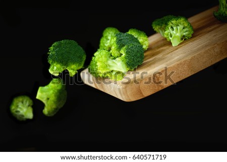 broccoli falling from cutting plate. Black background.