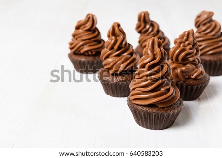 Some chocolate cupcakes with cocoa cream on white wooden table with copy space