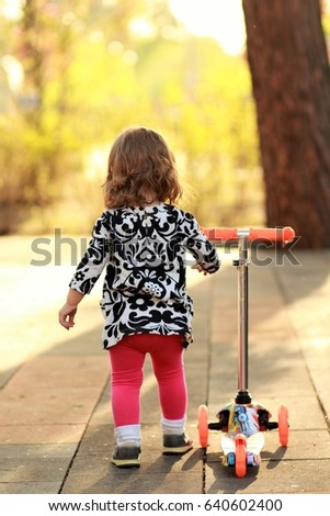 Cute little girl riding a scooter in the summer park, back view
