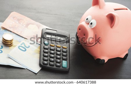 Piggy bank on banknotes and coins next to a calculator on black background. 