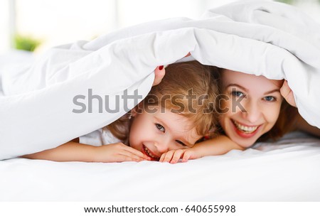 Happy family mother and child daughter play and laugh in bed
