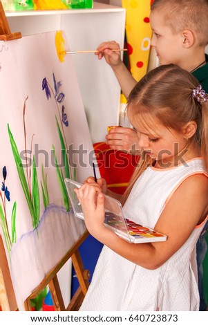 Children painting on easel. Girl with boy learn paint in class school. Child picture on background.