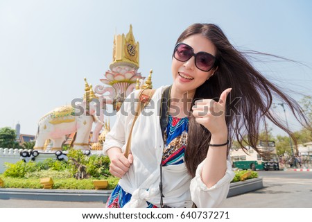 smiling female traveler standing in front of famous awesome Grand Palace building taking picture and making thumb up gesture face to camera on Bangkok, Thailand travel.
