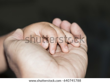 close up of  father holding child's hand over dark background