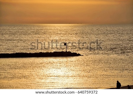 People walk the beach and a breakwater runs into Lake Michigan in New Buffalo, MI while a gorgeous springtime sunset reflects off the water, with view of Chicago skyline in the far distance.