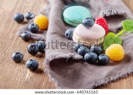 Traditional French sweets. Assorted colorful macaroons with mint green, white and red raspberries, blueberries. Dark wood background