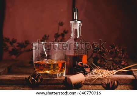 Glass of whiskey with ice decanter on wooden table.