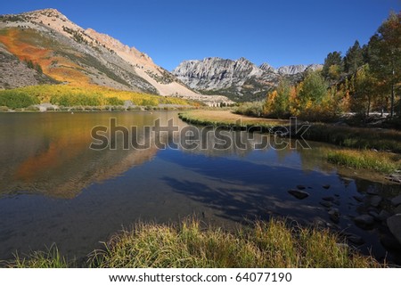 Bright autumn colors landscape. Mountains covered with orange and yellow bushes are reflected in the clean and clear water lakes