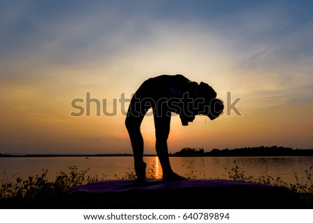 Black silhouette, beautiful mother and daughter are practicing yoga on rocks near the river. During the sunset and dusk.