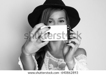 Beautiful girl taking self portrait with the phone, studio shot, black and white photo