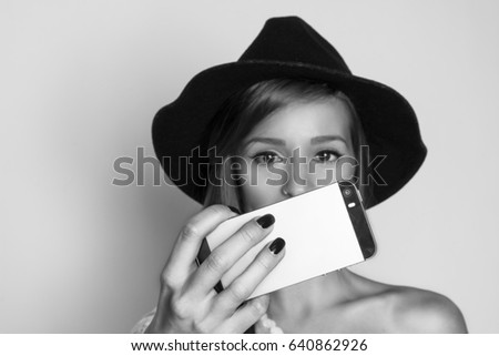 Beautiful girl taking selfie with smart phone, studio shot, black and white photo 