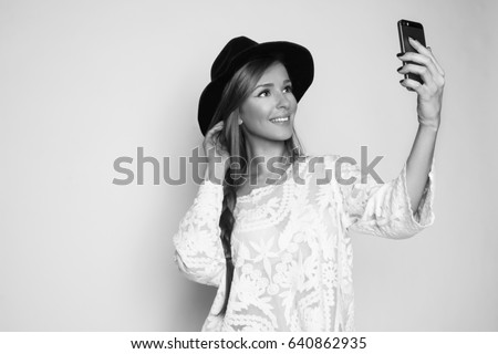 Beautiful girl smiling and taking selfie with the phone, studio shot, black and white photo