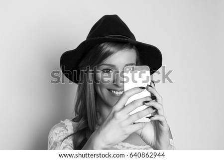 Smiling young woman taking photo with cellphone, studio shot, black and white photo 