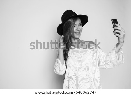 Happy smiled girl making selfie with the phone, studio shot, black and white photo