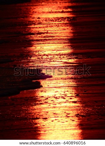 Abstract beach background of firey orange streaks of sunlight at sunset across golden sand and sea