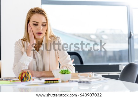 Stylish young woman sitting at table in office