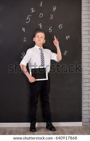 Handsome school boy in goggles white shirt tie standing close to school desk with numbers above around the head