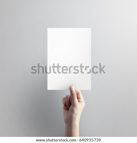 Woman hand holding blank paper sheet A5 size on grey background. Royalty-Free Stock Photo #640935739